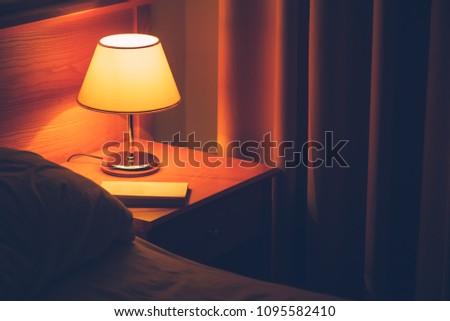 Book and vintage lamp on night table in hotel room. Retro styled bedroom interior.