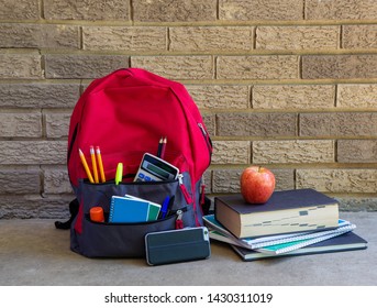 Bookbag With School Supplies And Stack Of Books Against A Brick Building With Copy Space