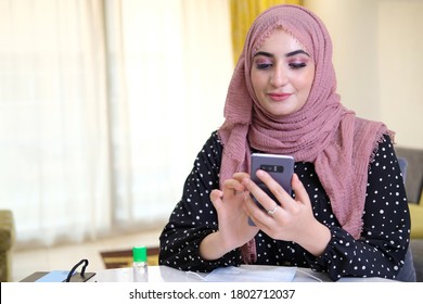 Booking Through Online By Arab Woman On Smart Mobile Phone On Headscarf Hijab. Emirati Girl Using Web Online Application. MIddle Eastern Lady Browing The Online Web Internet On Cellphone Device