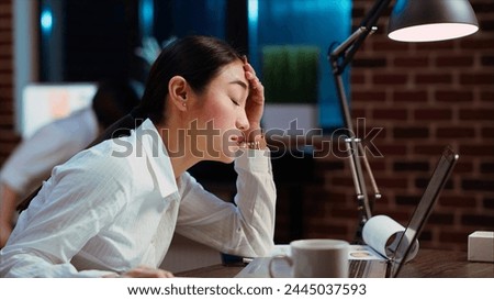 Bookkeeper feeling dread while having to do complicated tax reports in office at night. Worker squinting eyes in exasperation, feeling overworked while using laptop to do project research, camera B