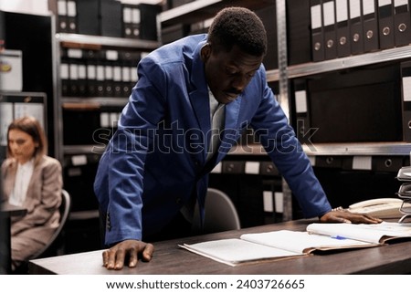 Bookkeeper working at bureaucracy report, analyzing administrative files late at night in storage room. African american businessman searching for bookkeeping record in corporate depository