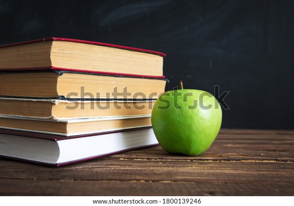 Books and apples on a wooden\
table against the background of the chalkboard or\
blackboard.