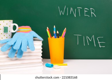 Books , Colored Pencil In Yellow Glass And Winter Gloves On Green Chalkboard. / End Of School. Winter Break