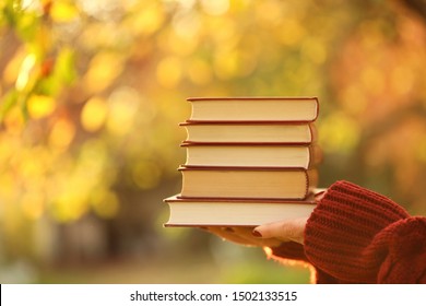 Books For The Fall.Autumn Book Sreading.Stack Of Books In Female Hands On Blurry Autumn Foliage In The Sunshine Background.Autumn Time.