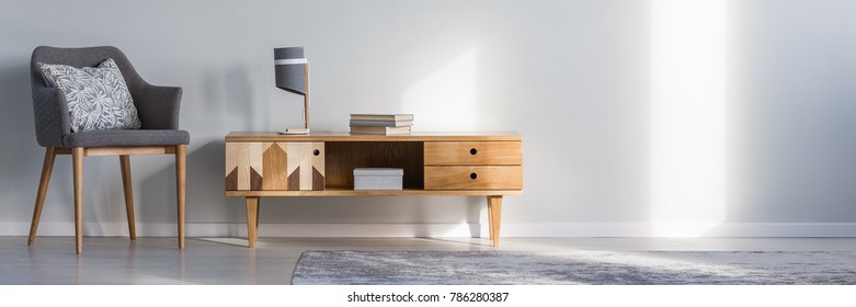 Books and lamp on rustic cupboard next to grey armchair with cushion against a wall with copy space in living room interior - Shutterstock ID 786280387