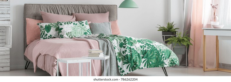 Books On White Table In Bright Bedroom With Green Lamp Above King-size Bed With Floral Bedding