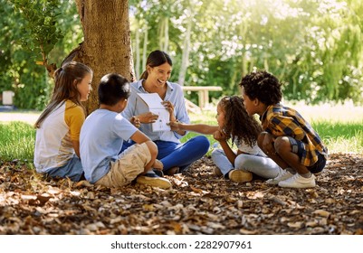 Books, reading or teacher with children in a park storytelling for learning development or growth. Smile, tree or happy educator with stories for education at a kids kindergarten school in nature - Powered by Shutterstock