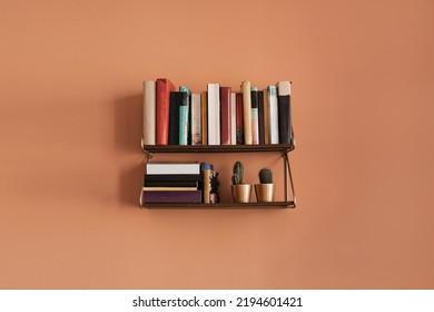 Books stack on hanging shelf. Coral peach wall background. Aesthetic minimal interior design. Reading, education concept with bookshelf