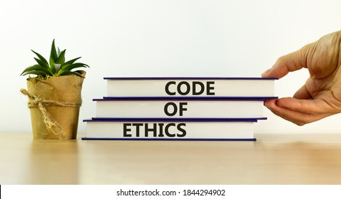 Books with text 'code of ethics' on beautiful wooden table, white background. Male hand and house plant. Business concept. Copy space. - Shutterstock ID 1844294902