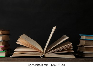 Bücher und ungefaltetes Buch auf braunem Holztisch und schwarzem Hintergrund. Alte Bücher. Bildung. Schule. Studie