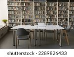 Bookshelves with heap of books on shelves, desk with laptop and copybooks in empty university library, no people. Place for studying, gain new knowledge, get professional skills or higher education