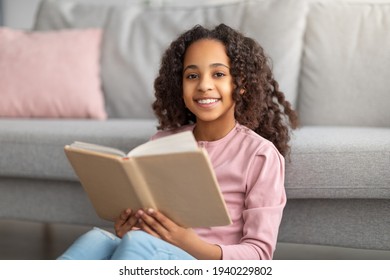 Bookworm. Cheerful Black Teen Girl Reading Paper Book, Resting At Home And Smiling To Camera