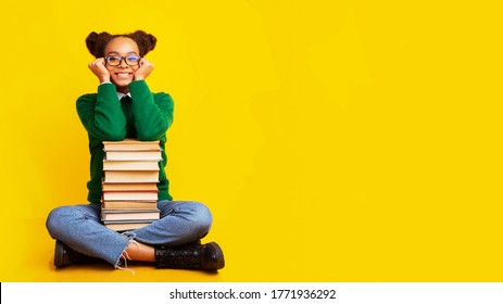 Bookworm. Dreamy afro teenage girl sitting on floor with pile of books over yellow background, copyspace, panorama