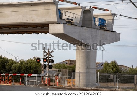 Boom Gates at a level crossing with a concrete bridge pier. House roof and fencing.