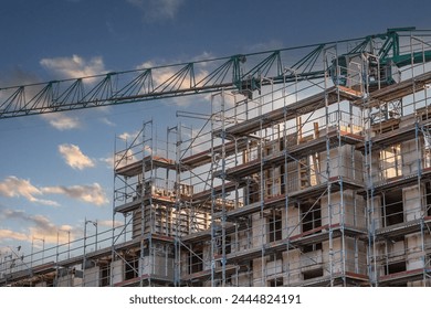 Boom of a green construction crane over the shell of an apartment building - Powered by Shutterstock