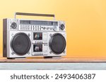 Boombox radio stereo cassette recorder on vintage wooden shelf front yellow background. Retro old style filtered photo