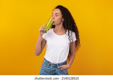 Boost Your Immune System Concept. Portrait of cool young lady holding glass drinking tasty green smoothie homemade from fresh ingredients with closed eyes, isolated on yellow orange studio wall - Shutterstock ID 2140128525