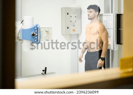 Booth interior photo of a young Caucasian man undergoing a chest x-ray test inside a hospital to detect cancer, infections or chronic lung diseases. X-ray x-ray concept