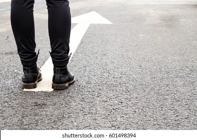 boots on a tarmac road with white direction arrow, the concept of moving forward