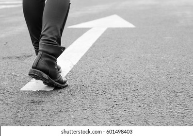 Boots On A Tarmac Road With White Direction Arrow, The Concept Of Moving Forward