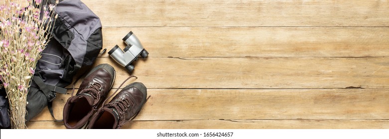 Boots For Trail, Backpack, Binoculars, Camping Equipment On A Wooden Background. The Concept Of Hiking, Tourism, Camp, Mountains, Forest. Banner. Flat Lay, Top View