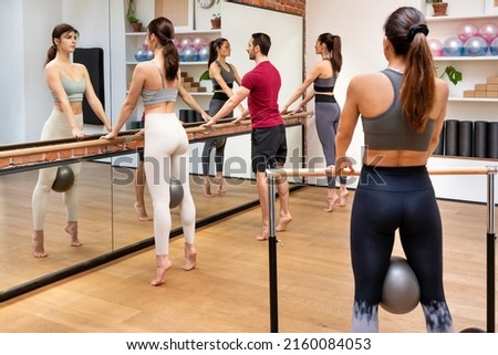 Booty barre fitness class standing near barre with balls and performing Releve exercise in spacious studio with mirror. Fitness class concept.
