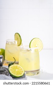 Boozy Classic Tequila  Margarita Refreshing Alcoholic Sweet And Sour Cocktail, With Lime,  Tequila, Green Chili Pepper. With Bar Accessories, Shaker, Ice Cubes On White Table