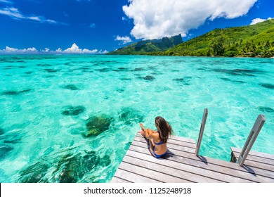 Bora bora luxury travel overwater bungalow resort vacation bikini woman at Tahiti hotel. Tropical exotic destination. Girl relaxing sitting on private balcony under the sun looking at ocean.