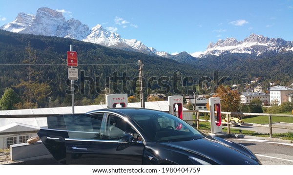 Borca di Cadore, Italy -\
October 12, 2020: A static shot of a solid black Tesla Model 3 dual\
motor long range awd charging at the Supercharger during\
autumn.