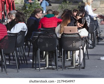 BORDEAUX, FRANCE - FEBRUARY 25, 2022: Selective Blur On A Young Woman Working Remotely Online With Her Apple Macbook Laptop At The Table Of A French Cafe On A Terrace In Bordeaux. 

