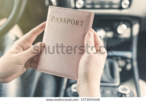 Border\
control concept.  Woman holding passport in a pink cover sitting on\
driver\'s seat in car for check customs\
officers