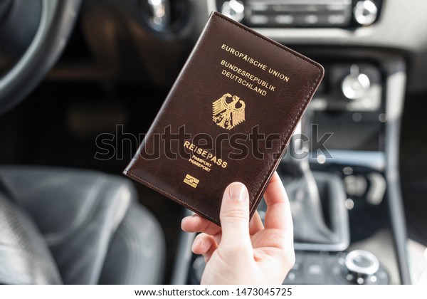 Border\
control concept.  Woman holding germany passport sitting on\
driver\'s seat in car for check customs\
officers