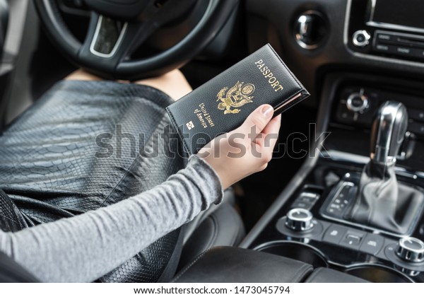 Border\
control concept.  Woman holding american passport sitting on\
driver\'s seat in car for check customs\
officers