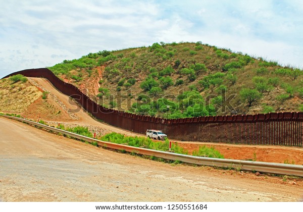 Border\
Fence beside a road near Nogales, Arizona separating the United\
States from Mexico with border patrol vehicle.\
