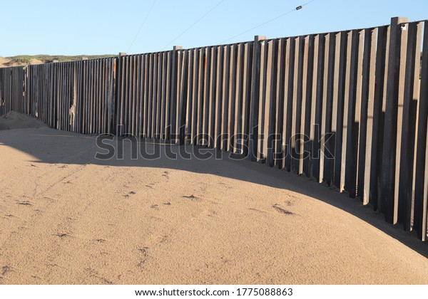 A border fence built on beach sand. Immigration\
control concept image. 