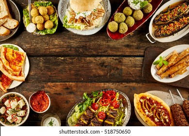 Border Of Mediterranean Dishes And Bread On Table. Copy Space In Middle Over Dark Wooden Surface.