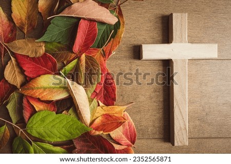 Border of rustic autumn leaves with a small wood cross on a wood background with copy space