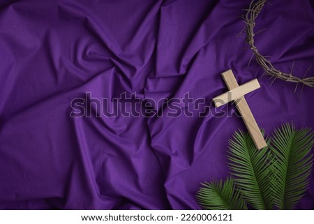 Border of wood cross, crown of thorns and palm leaves on a dark purple fabric background