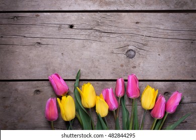 Border from yellow and pink spring tulips on vintage wooden background. Selective focus. Place for text.