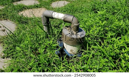 A bore well pump surrounded by lush green grass, often used in rural areas for groundwater extraction.