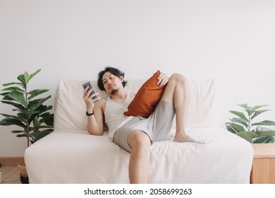 Bored Asian Man Relaxed And Use Smartphone For Killing Time Alone In Apartment.