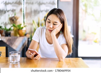Bored asian woman looking disappointed at her smart phone while waiting someone in restaurant