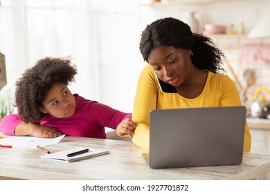 Bored Black Girl Demanding Attention From Her Busy Mom Working At Home, African American Freelancer Lady Using Laptop And Talking On Cellphone In Kitchen, Ignoring Her Lonely Child, Free Space