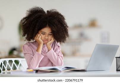 Bored Black Kid Schooler Suffering While Doing Homework, Tired From Studying At Home, Girl Getting Ready Before Exams, Using Laptop, Looking At Book, Copy Space. Home Education, Homeschooling Concept