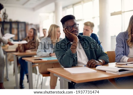 Bored black student sitting at university classroom and thinking of something. 