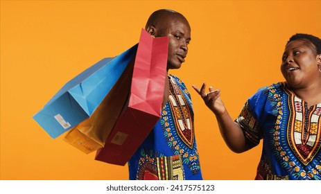 Bored boyfriend carrying shopping bags for his girlfriend, going to mall store to make her pleased and smiling. Excited happy woman buying products on sale, husband is suffering from exhaustion. - Powered by Shutterstock