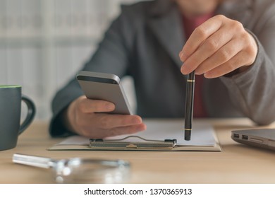 Bored Businesswoman Using Mobile Phone At Work To Waste Some Time Until Next Work Task