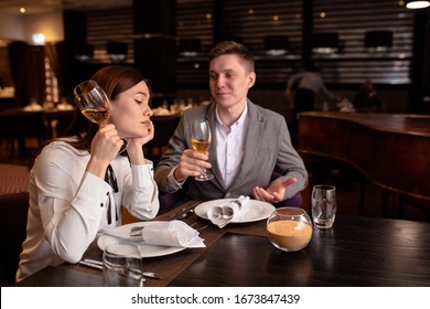 Bored Caucasian Woman With Champagne And Handsome Man Entertaining Her. Male In Love With Her, While Woman Is Not Interested In Rendezvous With Him. In Luxury Restaurant