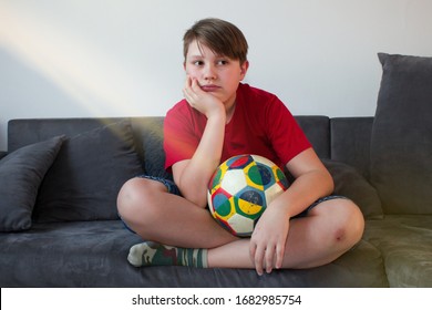 Bored child sitting on the couch and holding a football ball.Stay at home. Teenage boy bored sitting with kicking ball on couch. Quarantine due to coronavirus pandemic. - Powered by Shutterstock