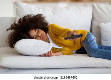 Bored Cute Curly African American School Girl Lying On Couch Alone, Holding Remote Controller, Black Kid Watching TV At Home, Switching Channels, Looking For Nice Cartoon, Copy Space